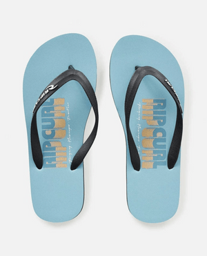 A pair of Rip Curl Surf Repeater Bloom Thongs in light blue, featuring ergonomic molded straps. "Rip Curl" and "Trippin’ Into Summer" are printed in blue and yellow on the footbeds.