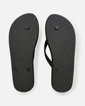 The Rip Curl Surf Repeater Bloom Thongs in black are shown from the bottom, highlighting their textured rubber soles with circular imprints, patterned grip tread, and an ergonomic molded strap for comfort.