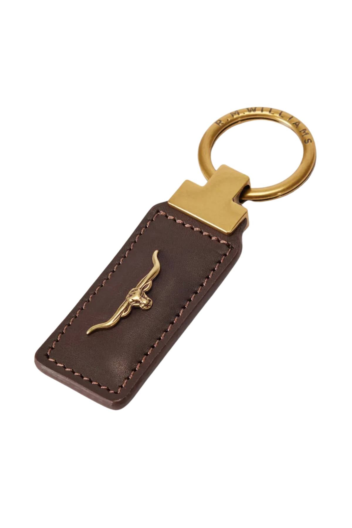 The RM Williams Angaston Key Ring is a brown smooth leather keychain with tan stitching, featuring a gold longhorn logo at the center and a brass key ring engraved with "R.M.WILLIAMS.