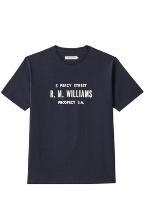 The RM Williams Bale T-Shirt is a navy blue regular-fit organic cotton tee with a front print reading "5 Percy Street R. M. Williams Prospect S.A." displayed on a plain white background.