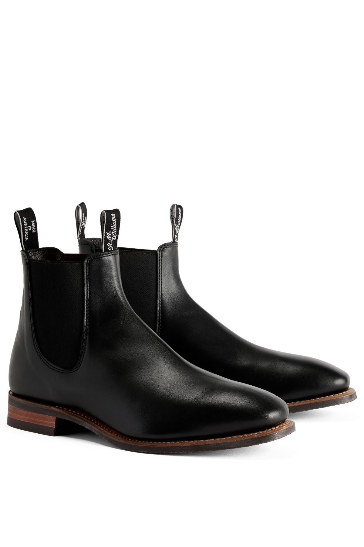The RM Williams Comfort Craftsman Boot is a black pull-up leather Chelsea boot with elastic side panels, pull tabs, comfort design, and brown stacked heels, shown against a white background.