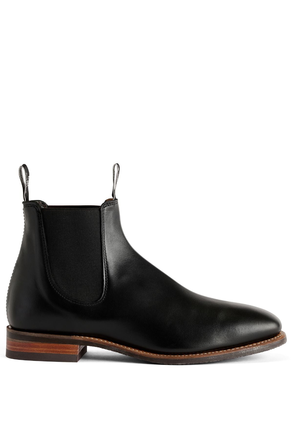 The RM Williams Comfort Craftsman Boot is a black pull-up leather Chelsea boot featuring elastic side panels, black pull tabs, and a brown stacked heel and sole, showcased in profile on a white background.