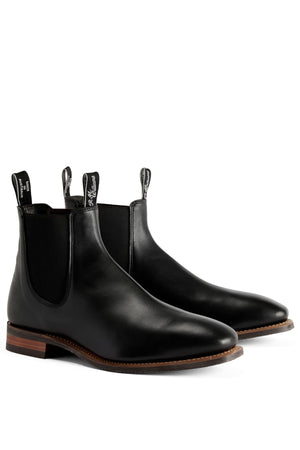 The RM Williams Comfort Craftsman Boot is a black pull-up leather Chelsea boot with elastic side panels, pull tabs, comfort design, and brown stacked heels, shown against a white background.