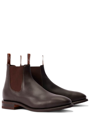 The RM Williams Comfort Craftsman Boot is a pair of dark brown handcrafted leather Chelsea boots with elastic side panels, fabric pull tabs, and low stacked heels—timeless style on a white background.