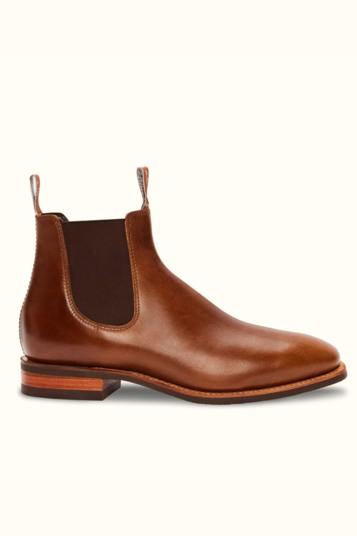 The RM Williams Comfort Craftsman Boot is a brown pull-up leather Chelsea boot with elastic side panels, front and back pull tabs, a low stacked heel, and a durable rubber sole, shown on a light background.