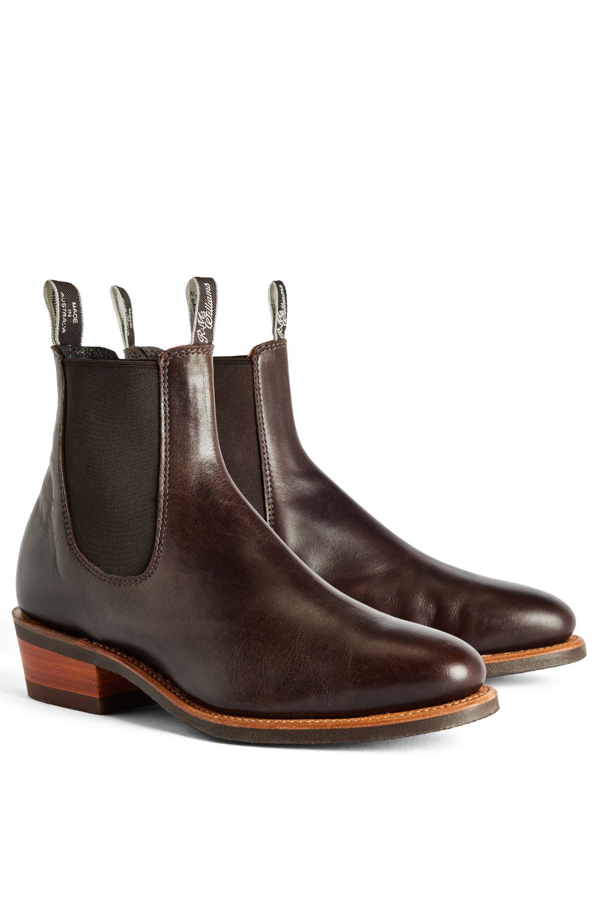 The RM Williams Comfort Lady Yearling Rubber Sole Boot is a women's dark brown leather Chelsea boot with elastic side panels, pull tabs, and low stacked heels, made in Australia and shown on a white background.