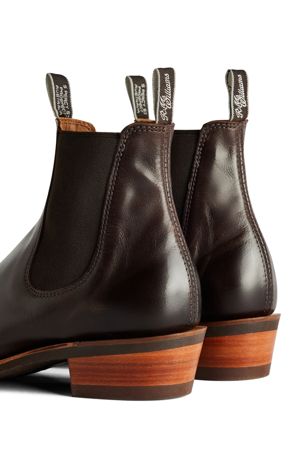 Close-up of the back and sides of two dark brown RM Williams Comfort Lady Yearling Rubber Sole Boots with black elastic panels, stacked wooden heels, and branded pull tabs. These stylish women's Chelsea boots are expertly made in Australia.