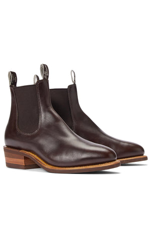 The RM Williams Comfort Lady Yearling Rubber Sole Boot is a dark brown pull-up leather Chelsea boot with elastic side panels, pull tabs, and stacked heels, featuring Goodyear welt construction and shown at an angle on a white background.