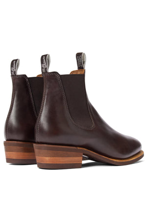 The RM Williams Comfort Lady Yearling Rubber Sole Boot is a pair of dark brown pull-up leather Chelsea boots with stacked wooden heels and black elastic side panels, shown from the back and slightly to the side.