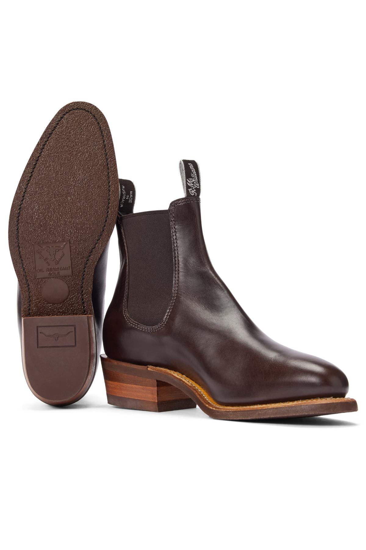 The RM Williams Comfort Lady Yearling Rubber Sole Boot is a pair of dark brown Chelsea boots in pull-up leather with elastic side panels, pull tabs, a textured rubber sole, wooden stacked heel, and Goodyear welt construction. One boot is upright; the other shows the sole.