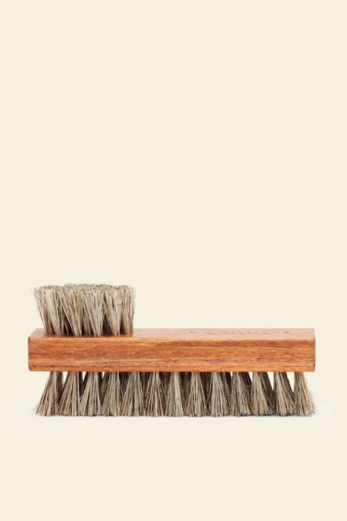 The RM Williams Double Sided Brush features natural bristles on both ends and a long wooden handle, ideal for boot care. Shown against a plain beige background, it has bristles on the bottom and a smaller cluster at the top.