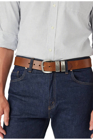 Close-up of a person wearing a light gray striped button-up tucked into dark blue jeans, finished with the RM Williams Drover Belt in premium brown leather and an antique silver buckle. Their hands rest casually at their sides.