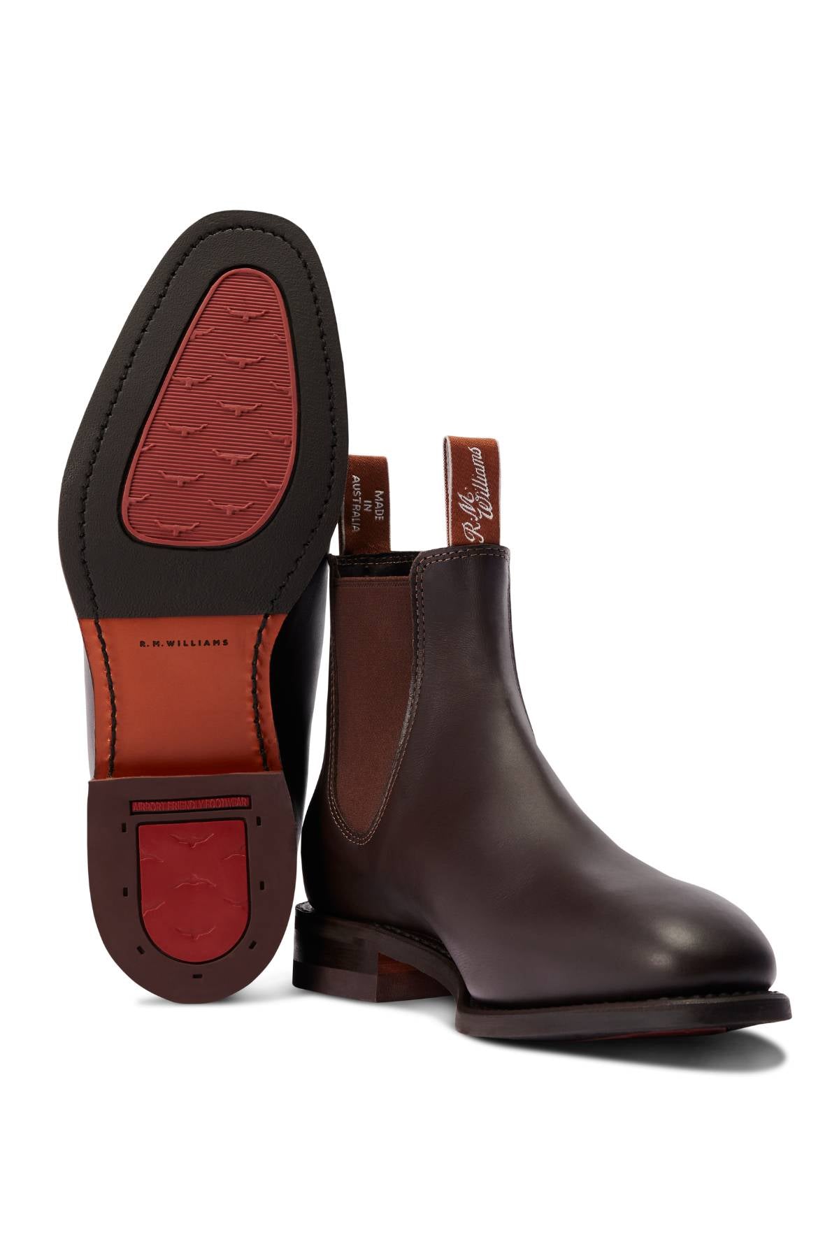 The RM Williams Dynamic Flex Craftsman Boot in dark brown yearling leather features brown elastic side panels and pull tabs; one boot stands upright while the other displays its textured sole and heel—classic handcrafted style.