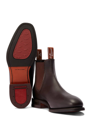 The RM Williams Dynamic Flex Craftsman Boot in dark brown yearling leather features brown elastic side panels and pull tabs; one boot stands upright while the other displays its textured sole and heel—classic handcrafted style.