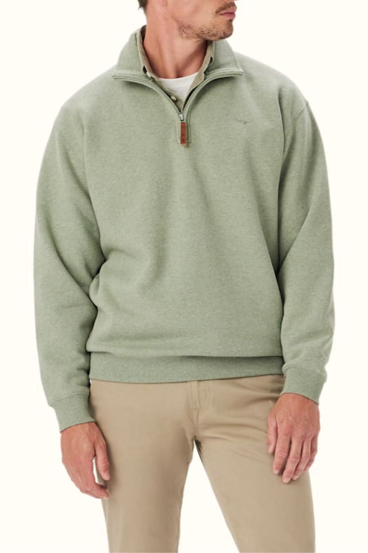 A man in the RM Williams Mulyungarie Fleece—a light green organic cotton blend quarter-zip with a leather zipper pull and subtle Longhorn embroidery—pairs it with khaki pants, standing against a plain background, head turned slightly to the side.