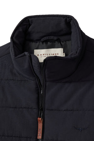 Close-up of the RM Williams Patterson Creek Jacket in black recycled nylon, lightweight and quilted, with a high collar, partial zipper featuring a brown leather pull, "R.M. Williams" inner label, and embroidered chest logo visible.