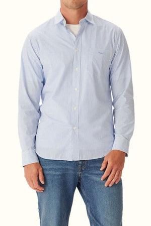 A man stands against a plain background wearing the RM Williams Regular Poplin Stripe Shirt in light blue and white over a white t-shirt, paired with blue jeans.