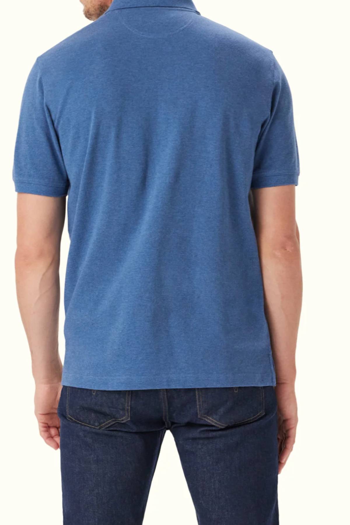 A man is shown from the back, wearing the RM Williams Rod Polo—short-sleeved, blue, organic cotton with subtle Longhorn embroidery—and dark jeans against a plain light background.