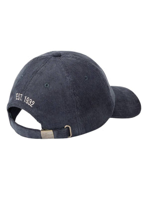 The RM Williams Script Longhorn Cord Cap is a dark blue organic cotton corduroy baseball cap, shown from the back with an adjustable strap and metal buckle. "EST. 1932" is embroidered in white above the opening for a classic touch.