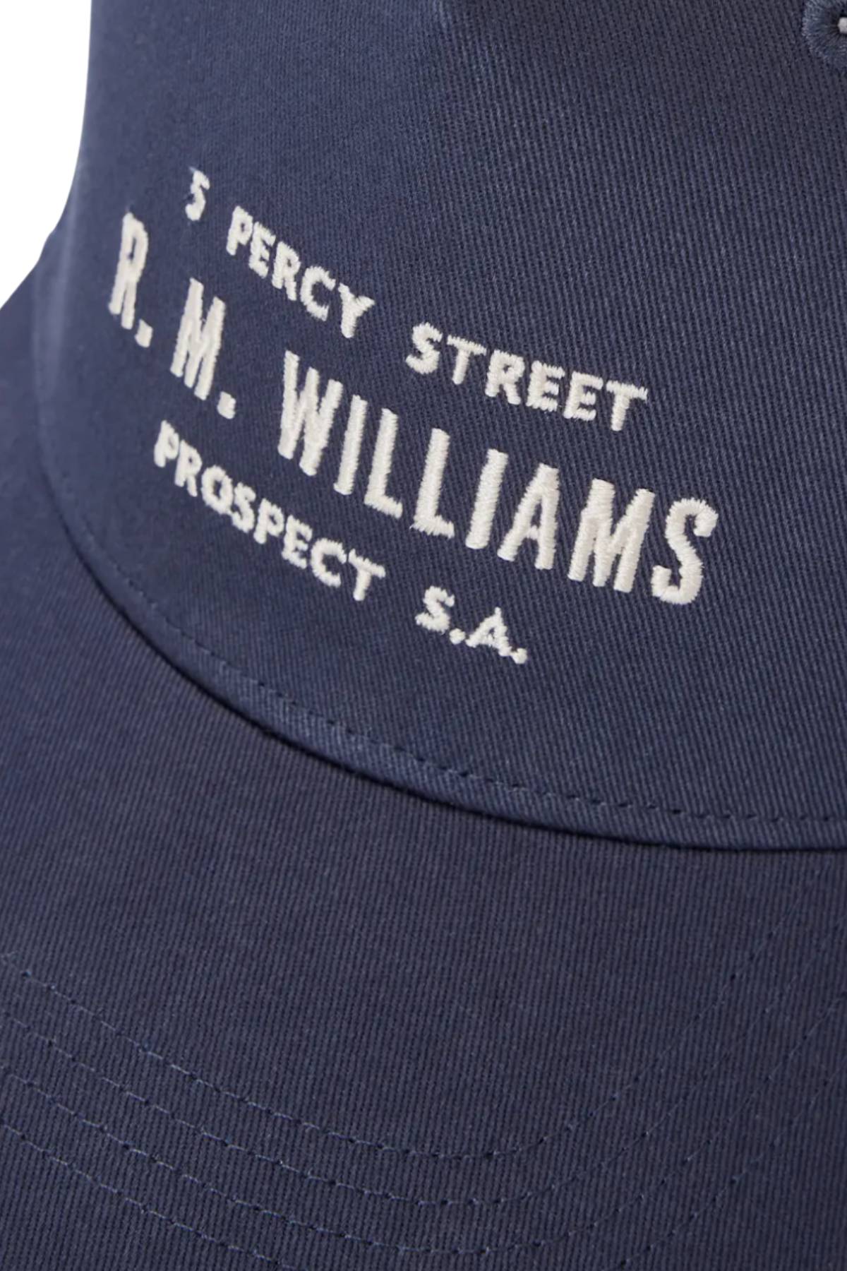 Close-up of the RM Williams Stencil Trucker Cap in navy organic cotton twill, featuring white embroidered text: "3 Percy Street, R.M. Williams, Prospect S.A.