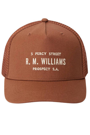 The RM Williams Stencil Trucker Cap features brown mesh, organic cotton twill, a white "5 PERCY STREET R. M. WILLIAMS PROSPECT S.A." stencil graphic on the front, and a classic snapback adjuster for a perfect fit.