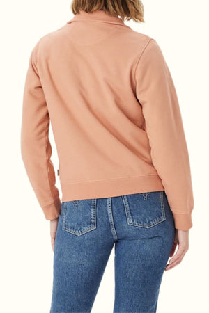 A person is seen from the back against a plain light background, wearing an RM Williams Trickett Zip Neck Sweatshirt in light pink organic cotton with blue jeans.