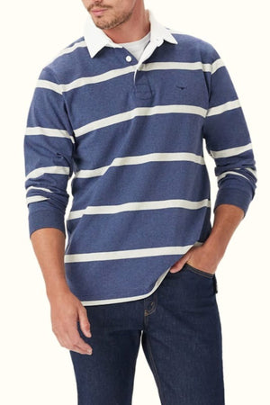 A man wearing the RM Williams Tweedale Rugby— a heavyweight cotton blue and white striped long-sleeve shirt with a white collar—pairs it with dark jeans, standing with one hand in his pocket against a plain background.
