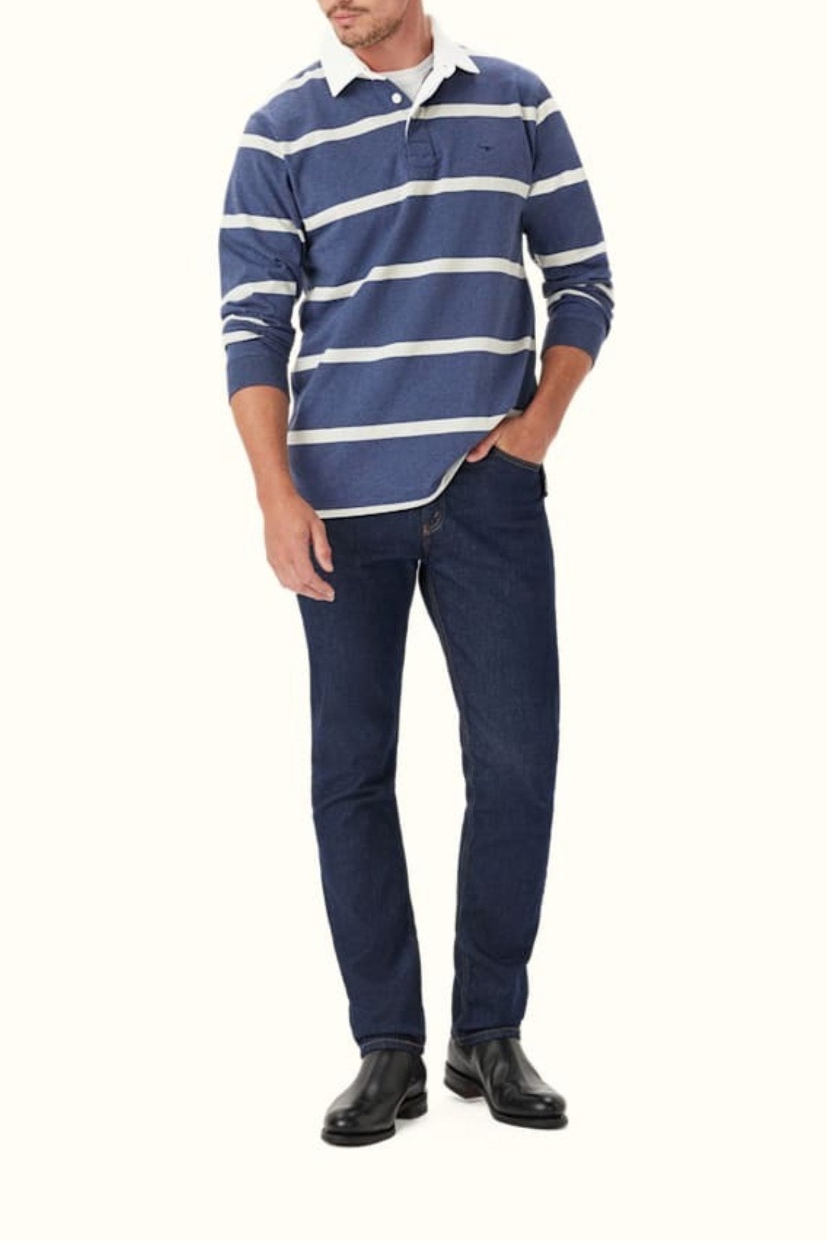Wearing the RM Williams Tweedale Rugby—a blue and white striped heavyweight cotton shirt—with dark blue jeans and black shoes, a man stands with one hand in his pocket against a light background.