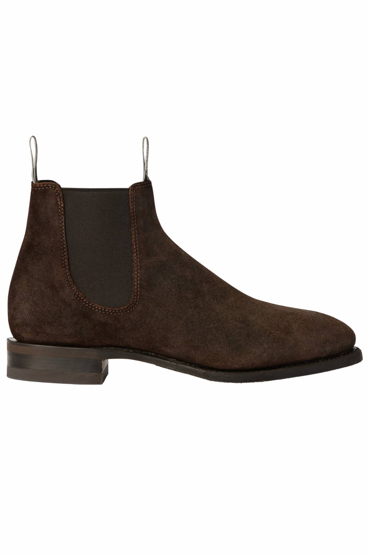 The RM Williams Comfort Craftsman Boot is a dark brown waxed suede Chelsea boot with elastic side panels, white pull tabs, and a low stacked heel, shown in side profile against a white background.