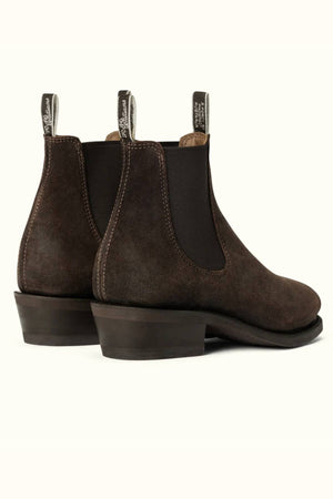 The RM Williams Comfort Lady Yearling Boot is a pair of dark brown waxed suede Chelsea boots with black elastic side panels, pull tabs, stacked heels, and Goodyear welt construction, shown against a light background.