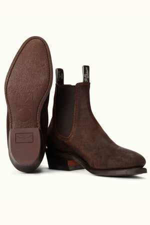 The RM Williams Comfort Lady Yearling Boot is a pair of brown waxed suede Chelsea boots with elastic side panels, pull tabs, textured sole, heel detail, and classic Goodyear welt construction. One boot stands upright; the other shows the sole.