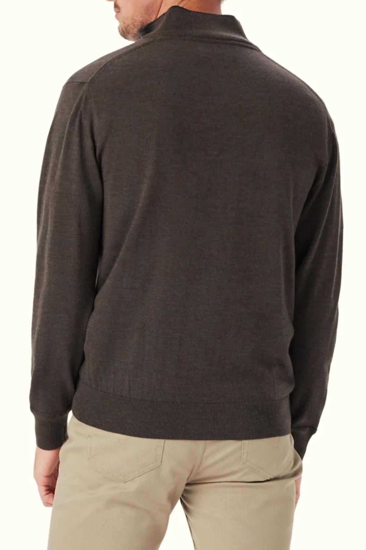 A man wearing an RM Williams Ernest 1/4 Zip Merino Knit sweater in dark brown and beige pants stands with his back to the camera against a plain light background.
