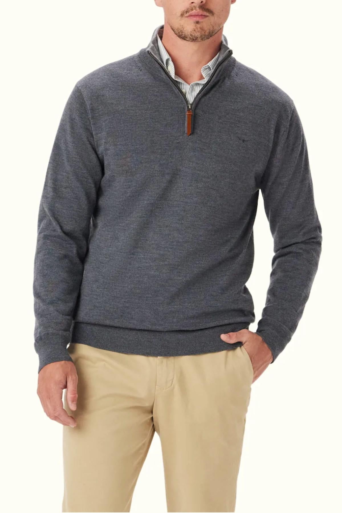 A man stands against a plain light background, wearing the RM Williams Ernest 1/4 Zip Merino Knit sweater over a collared shirt and beige pants, with one hand in his pocket.