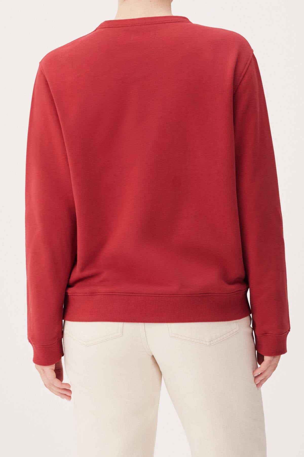 A person is seen from the back with arms relaxed, wearing the RM Williams Heritage Brushed Sweatshirt in plain red and light beige pants.