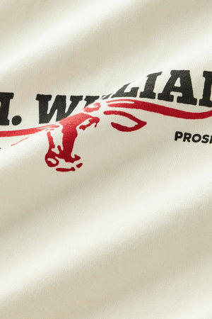 A close-up of the RM Williams Holt Tee’s white fabric, featuring bold black text and a red outline drawing of a donkey’s head. Some partially visible text reads “…WILLIAMS” and “PROS…”.