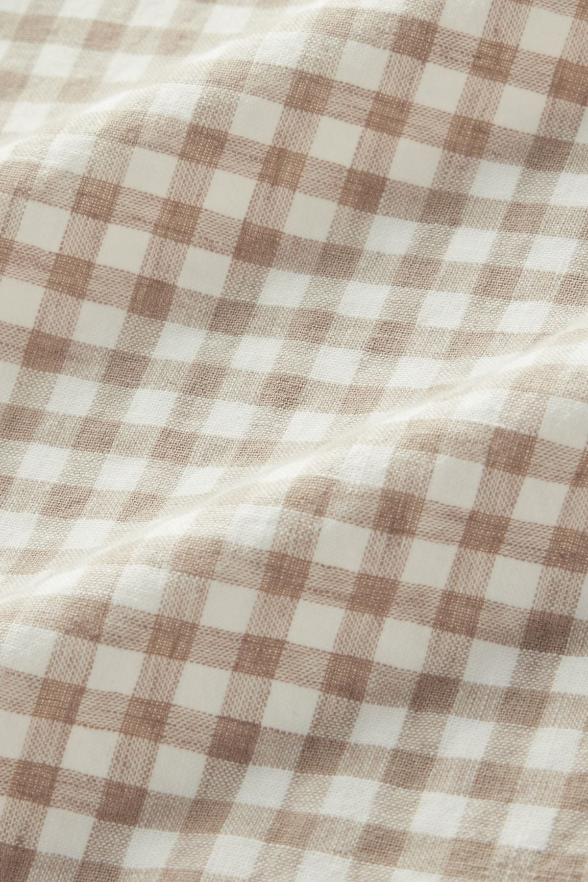 The RM Williams Johnson Check Short Sleeve Shirt features a beige and white gingham fabric with a soft texture, displaying a checkered pattern and gentle folds across the surface.