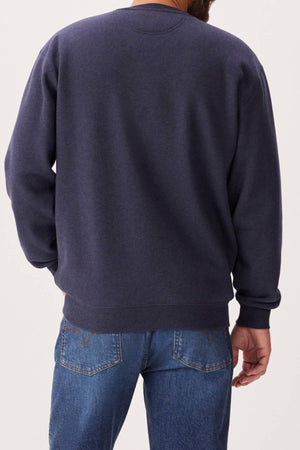 A person is seen from the back wearing an RM Williams Mini Longhorn Sweatshirt in dark blue with blue jeans, standing against a plain light background.