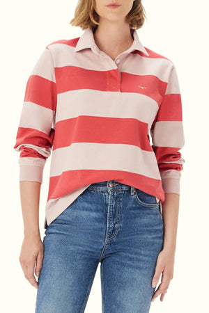 A woman wears the RM Williams Narran Stripe Rugby, a heavyweight jersey shirt with wide red and light pink stripes, slightly front-tucked into blue jeans with her right hand in her pocket.