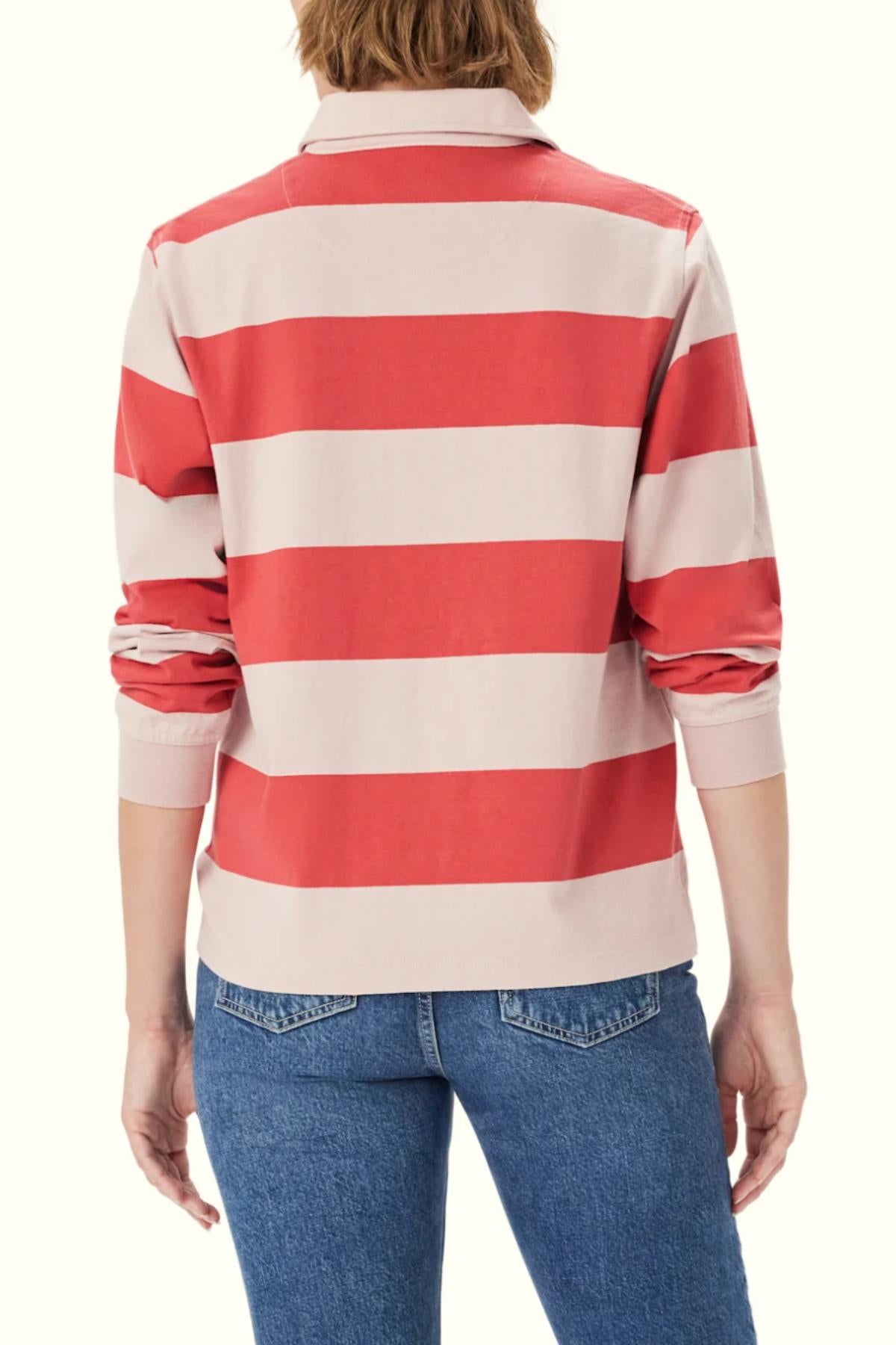 Someone, seen from the back, is wearing the RM Williams Narran Stripe Rugby—a heavyweight jersey long-sleeve shirt with wide red and light pink horizontal stripes—paired with blue jeans.