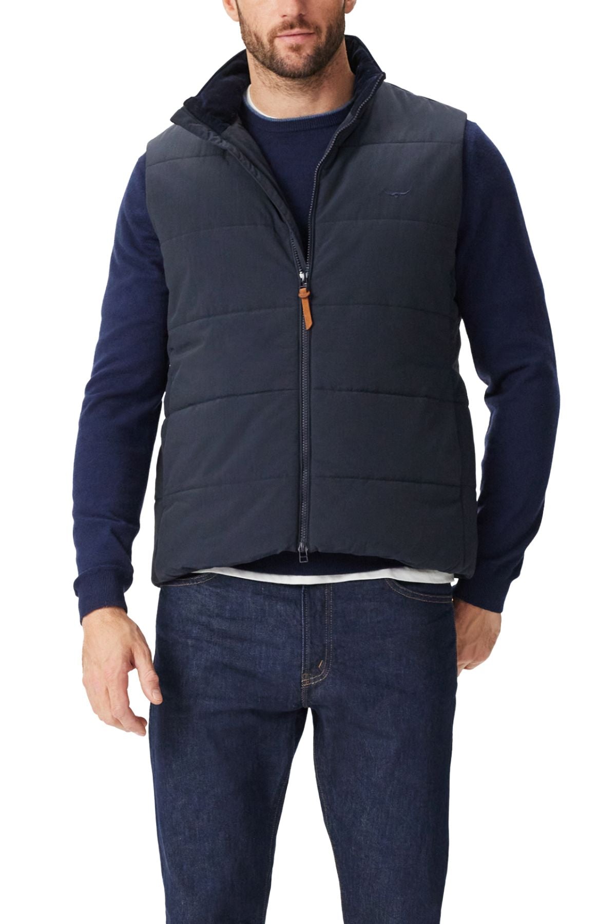 A man wearing an RM Williams Padstow Vest over a navy long-sleeve shirt and blue jeans stands facing forward with his left hand in his pocket.
