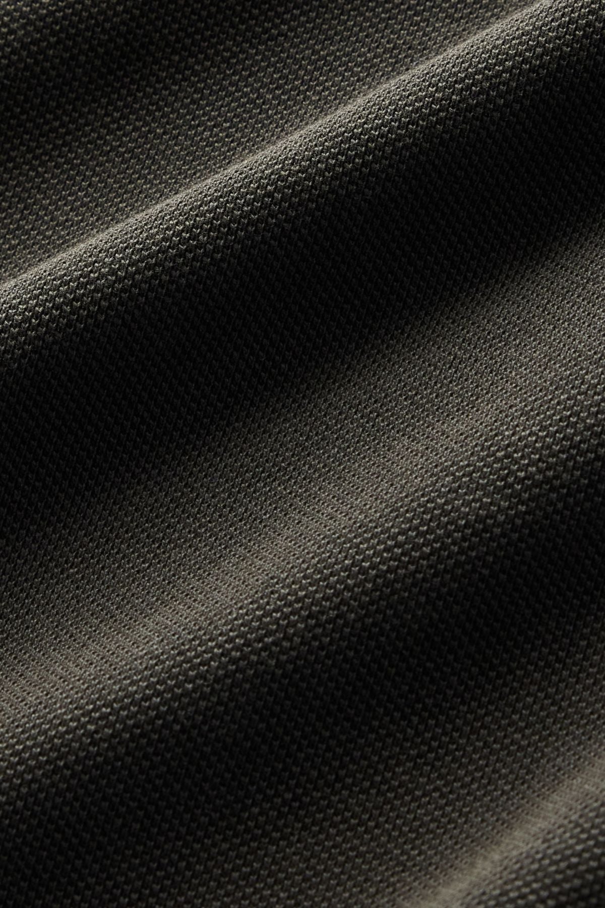 Close-up of the RM Williams Rod Polo in dark gray, featuring textured fabric with diagonal waves and a subtle grid-like pattern, highlighting the fine weave detail and shadowing from the folds.