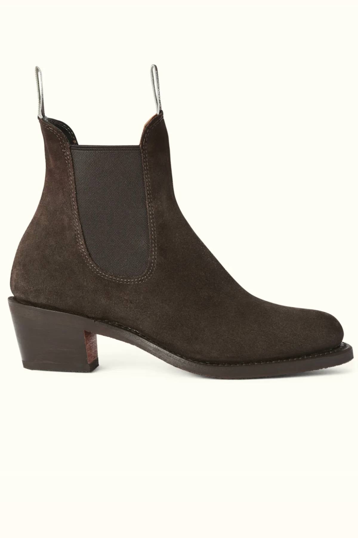 The RM Williams Rosebery Boot is shown in side profile on a light background, featuring dark brown suede leather, a low tapered block heel, elastic side panels, and front and back pull tabs.