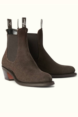 The RM Williams Rosebery Boot is a pair of brown suede leather Chelsea boots, featuring elastic side panels, pull tabs, and stacked wooden heels, shown against an off-white background.