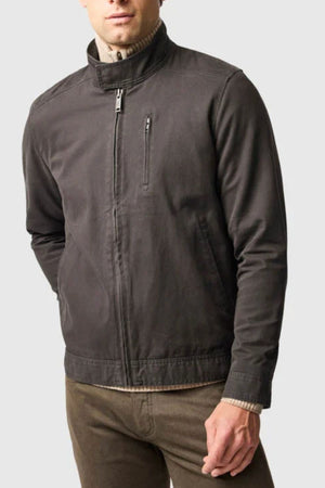 A man wears a dark gray Rodd & Gunn Armitage Jacket with YKK zips and a stand collar, paired with brown pants, standing against a plain light gray background.