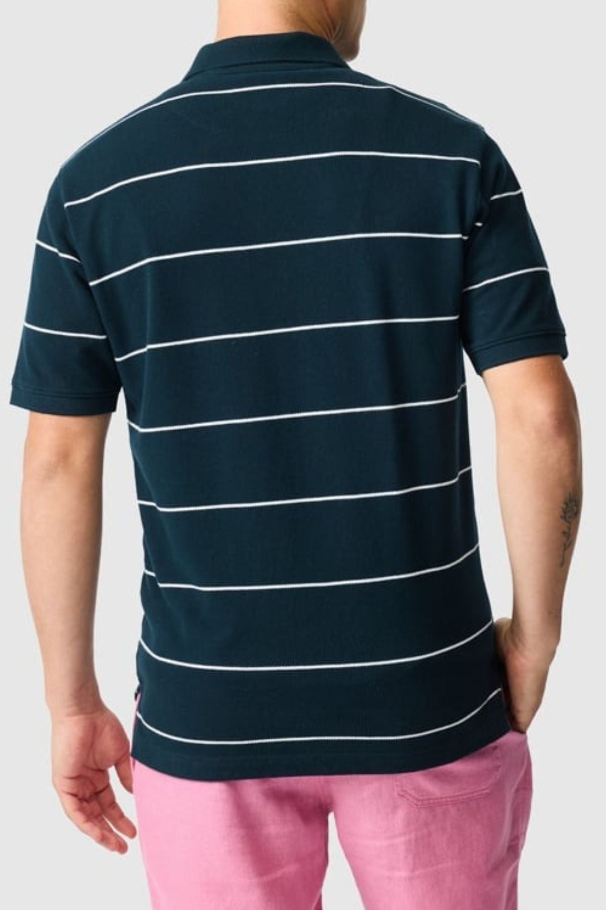 A person is seen from the back against a light gray background wearing a Rodd & Gunn Glen Eden Polo with white horizontal stripes and a high-retention rib collar, paired with pink shorts.