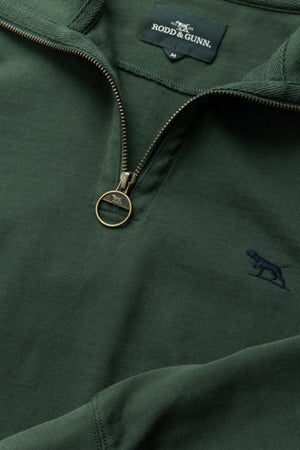 Close-up of the Rodd & Gunn Gunn 14oz 1/4 Zip Sweat in green, made from 100% Australian Good Earth Cotton with FibreTrace®. Visible details include a metallic zipper, embroidered dog logo, and inner brand label.