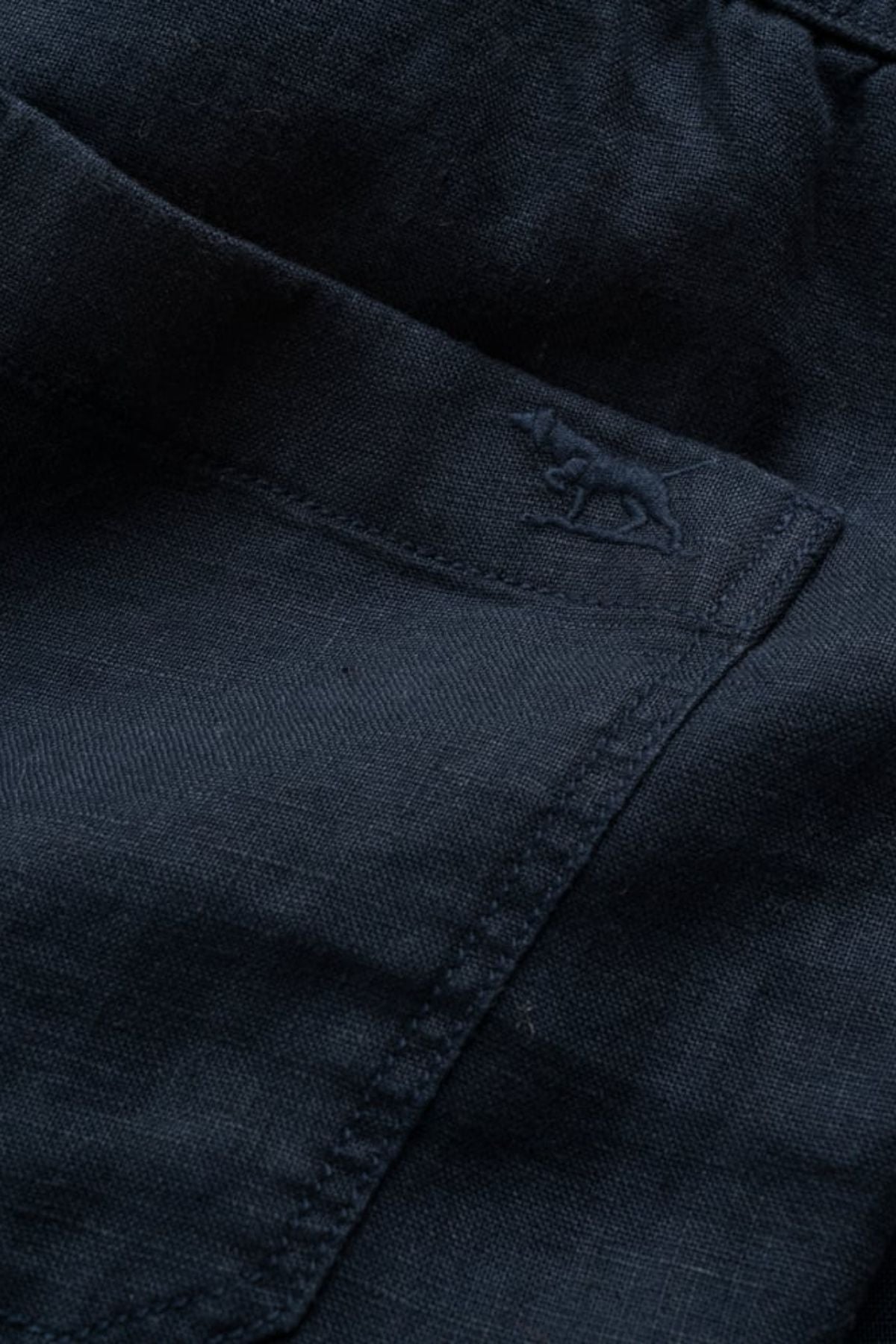 Close-up of a dark blue pocket on the Rodd & Gunn Linen Resort Short, featuring subtle stitching and an embroidered rhinoceros logo near the pocket opening.