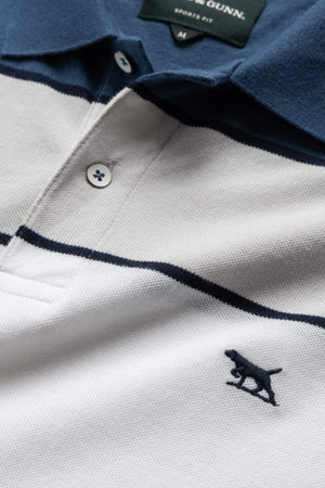 The Rodd & Gunn McLeod Bay Sports Fit Polo features a close-up of a cotton fabric with navy and white horizontal stripes, a navy collar, and pique texture. An embroidered dog silhouette adorns the lower right side. The label indicates "Small Fit.