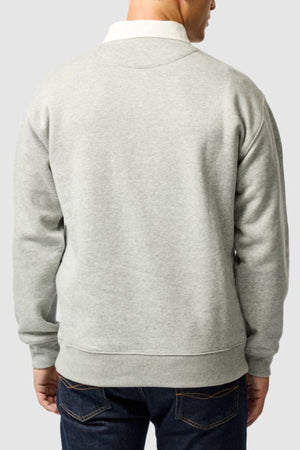 A person is shown from the back, wearing the Rodd & Gunn Otago Sweat with a traditional twill rugby collar over a white shirt and dark blue jeans, standing against a plain light gray background.