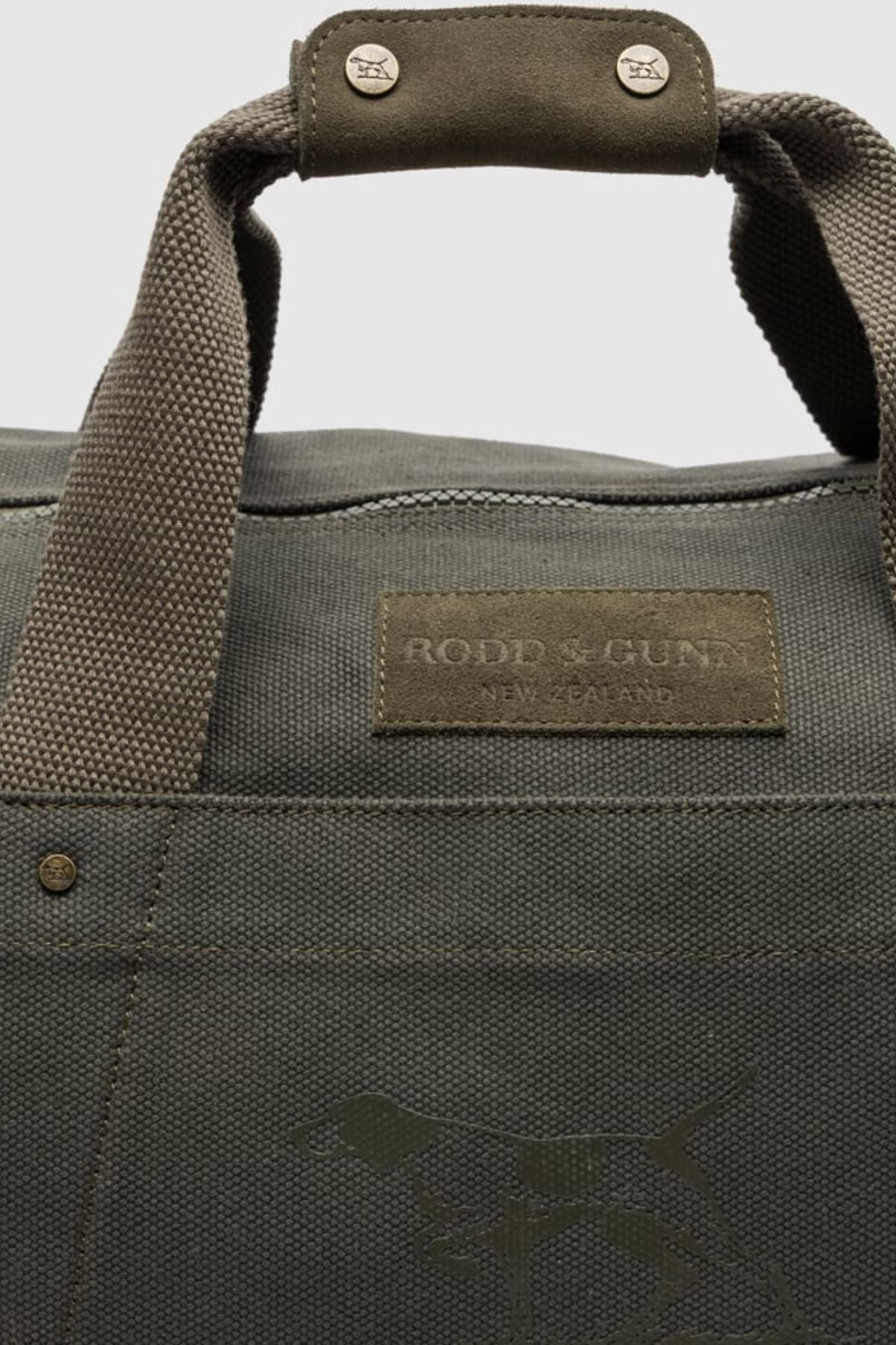 Close-up of the Rodd & Gunn Ponsonby Road Duffle Bag in olive green cotton canvas, featuring sturdy handles, a stitched leather patch with "RODD & GUNN NEW ZEALAND," and an embossed dog outline near the bottom.